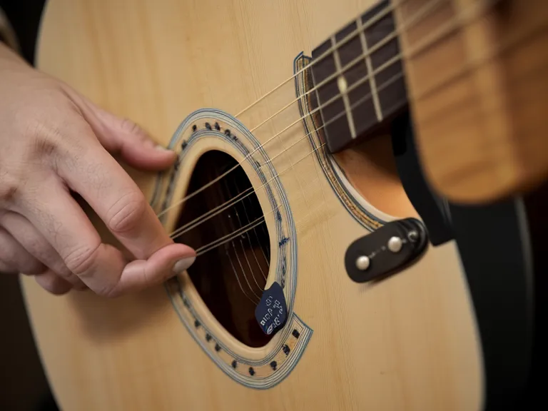 Dedos presionando las cuerdas de una guitarra acústica al practicar independencia de los dedos en acordes difíciles