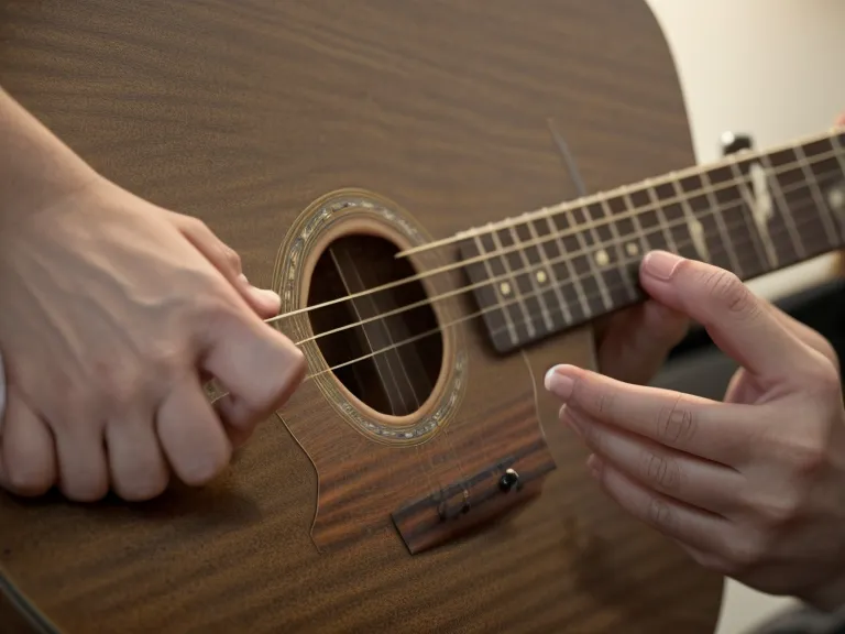 Metrónomo mecánico sobre una mesa de madera junto a una púa, usado para practicar el ritmo en la guitarra acústica