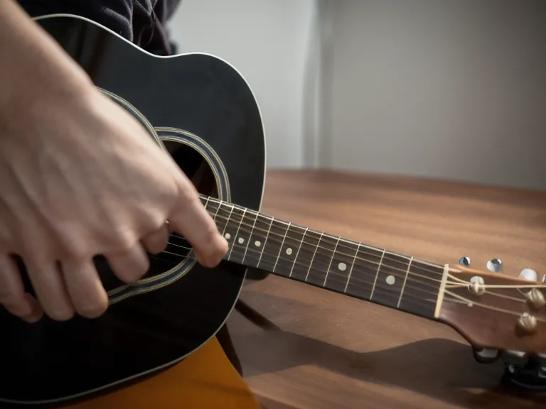 Dedos de un principiante adulto formando el acorde de Fa mayor durante la práctica de guitarra cristiana