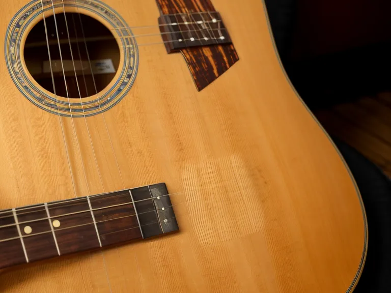 Guitarra acústica de adulto principiante apoyada en un sillón, escena de aprender guitarra y progreso musical en casa